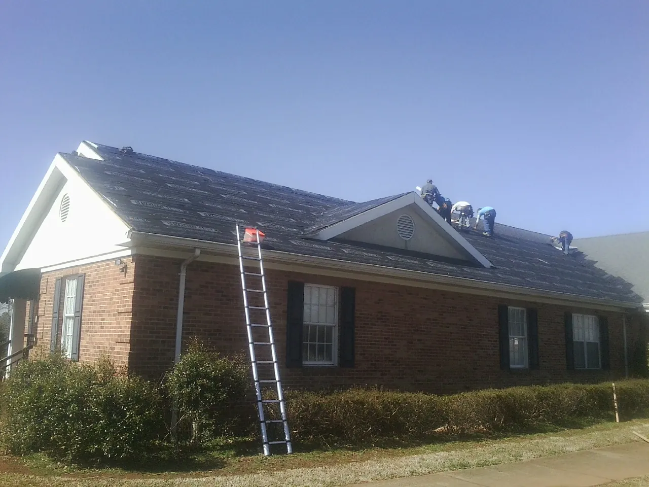 Crew tearing shingles off a brick ranch roof with a ladder set — Emergency Roof Repair work by our crew in Germantown