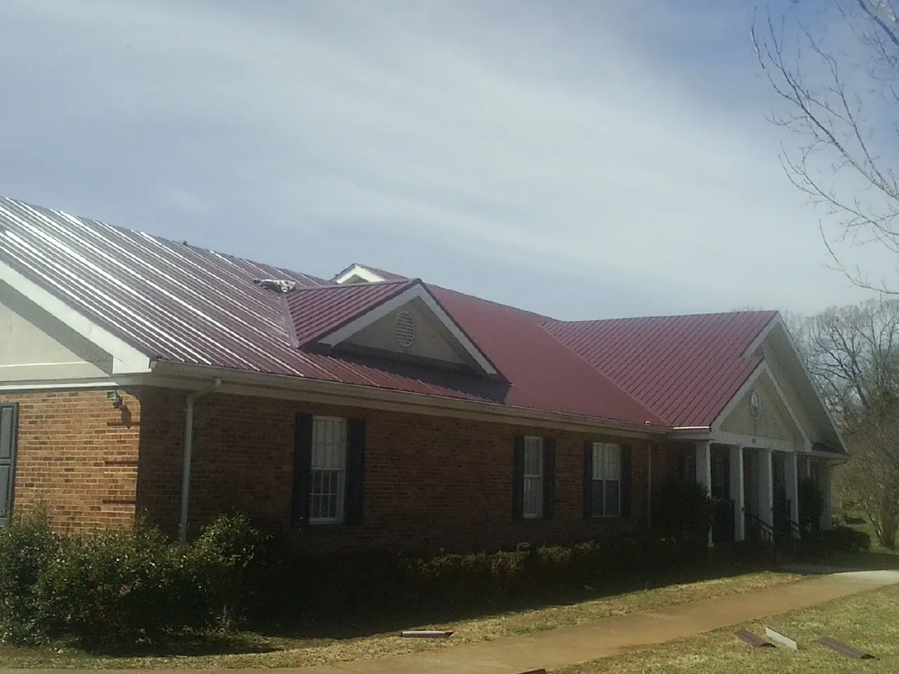 Red metal roof with gabled entries on a long brick building, from a Hail Damage Roof Repair job in Germantown