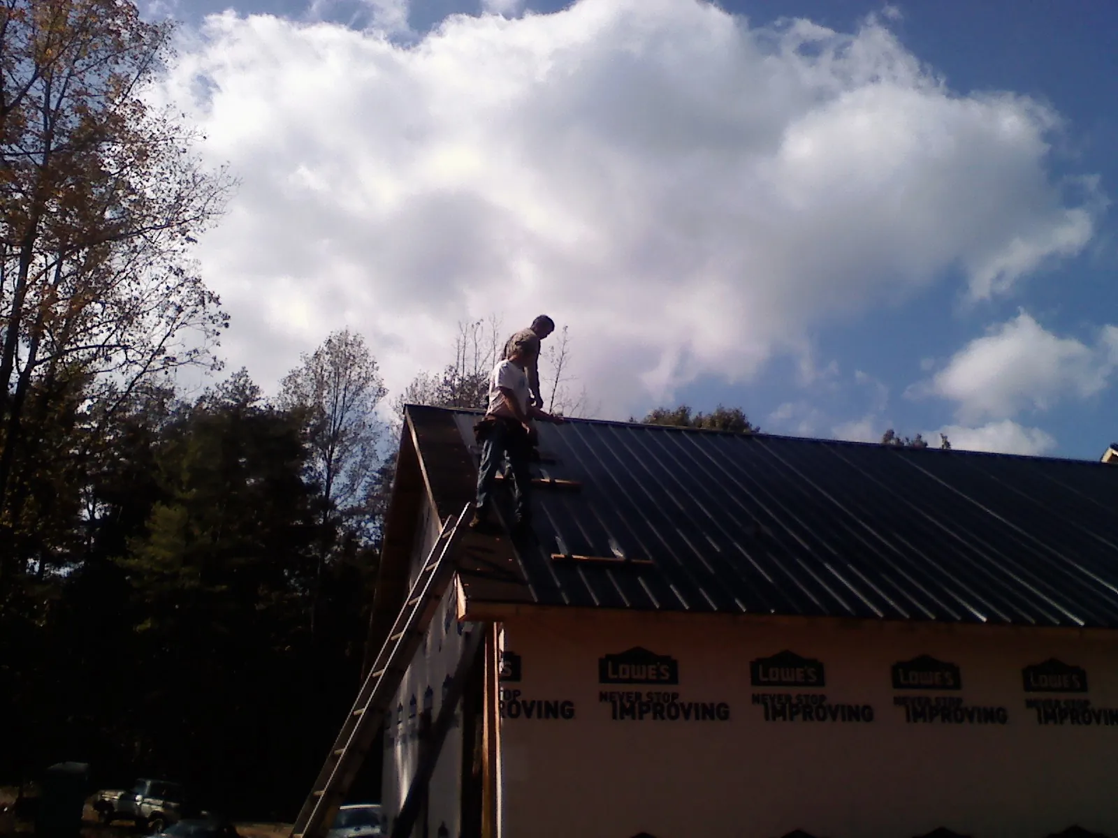 Roofer fastening dark metal panels high against a cloudy sky, from a Roof Inspection job in Germantown